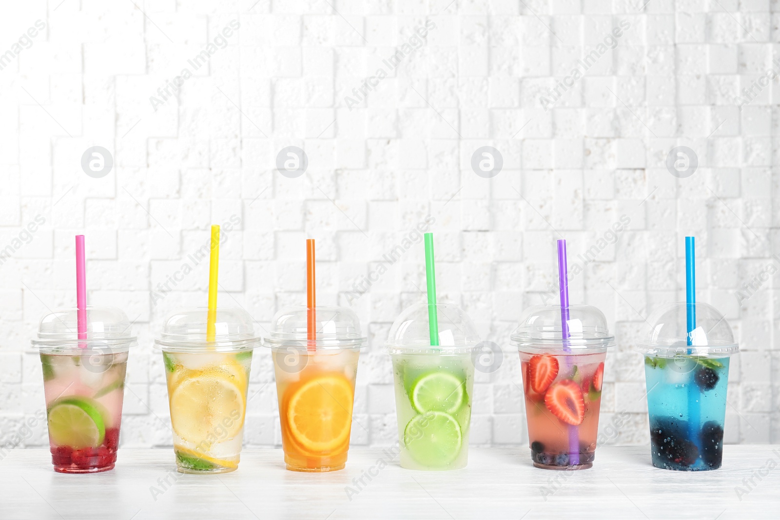 Photo of Plastic cups with lemonades on table near white wall