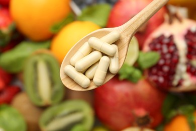 Photo of Vitamin pills in spoon over fresh fruits, top view