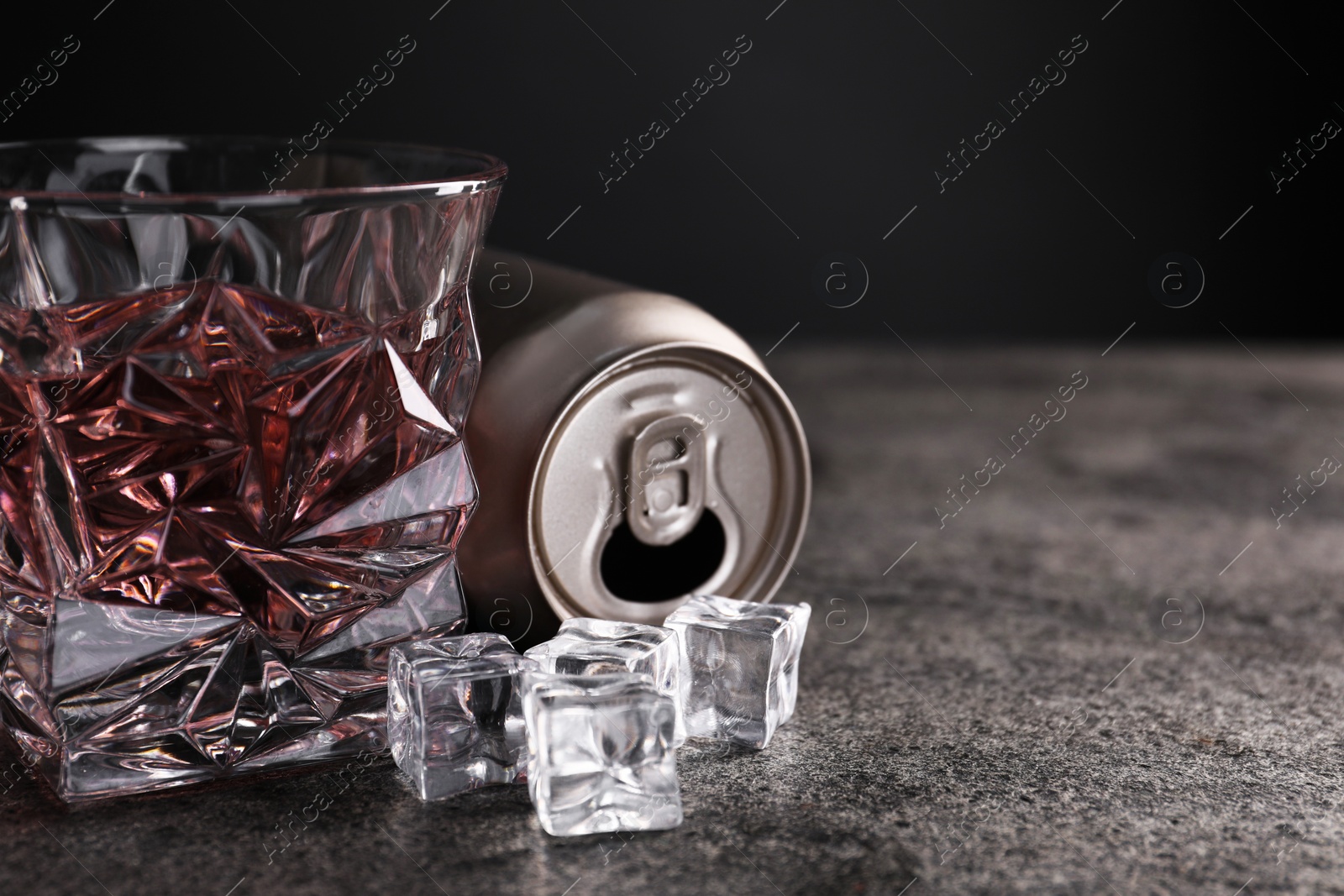 Photo of Energy drink in glass, aluminium can and ice cubes on grey table, closeup. Space for text