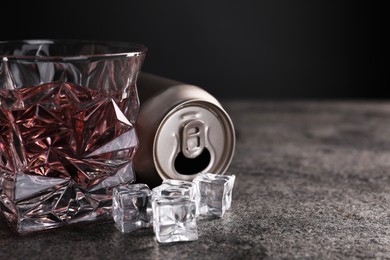 Energy drink in glass, aluminium can and ice cubes on grey table, closeup. Space for text