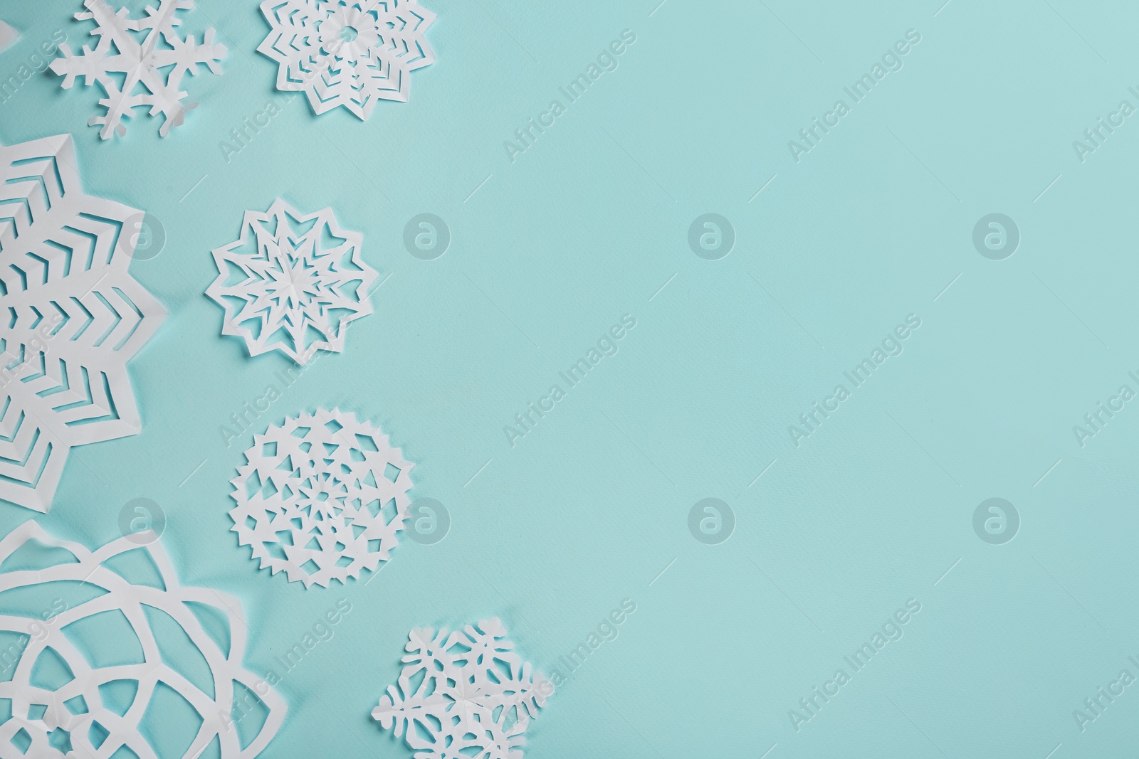 Photo of Flat lay composition with paper snowflakes on cyan background. Space for text