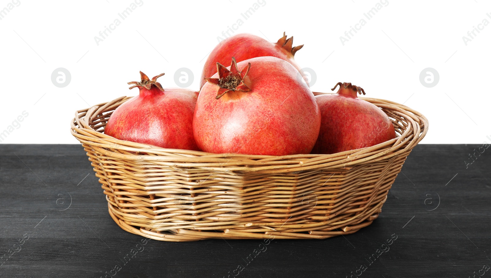 Photo of Fresh pomegranates in wicker basket on black wooden table against white background