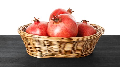 Photo of Fresh pomegranates in wicker basket on black wooden table against white background