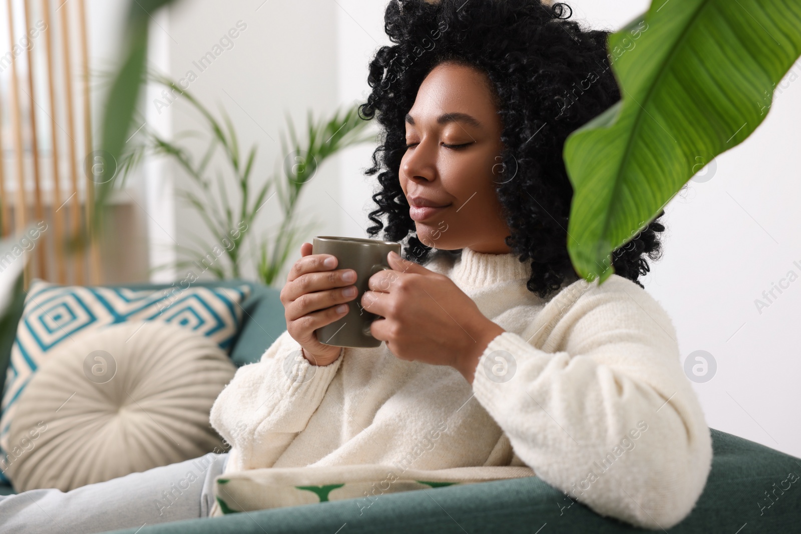 Photo of Relaxing atmosphere. Woman with cup of hot drink near beautiful houseplants in room