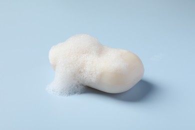 Photo of Soap with fluffy foam on light blue background