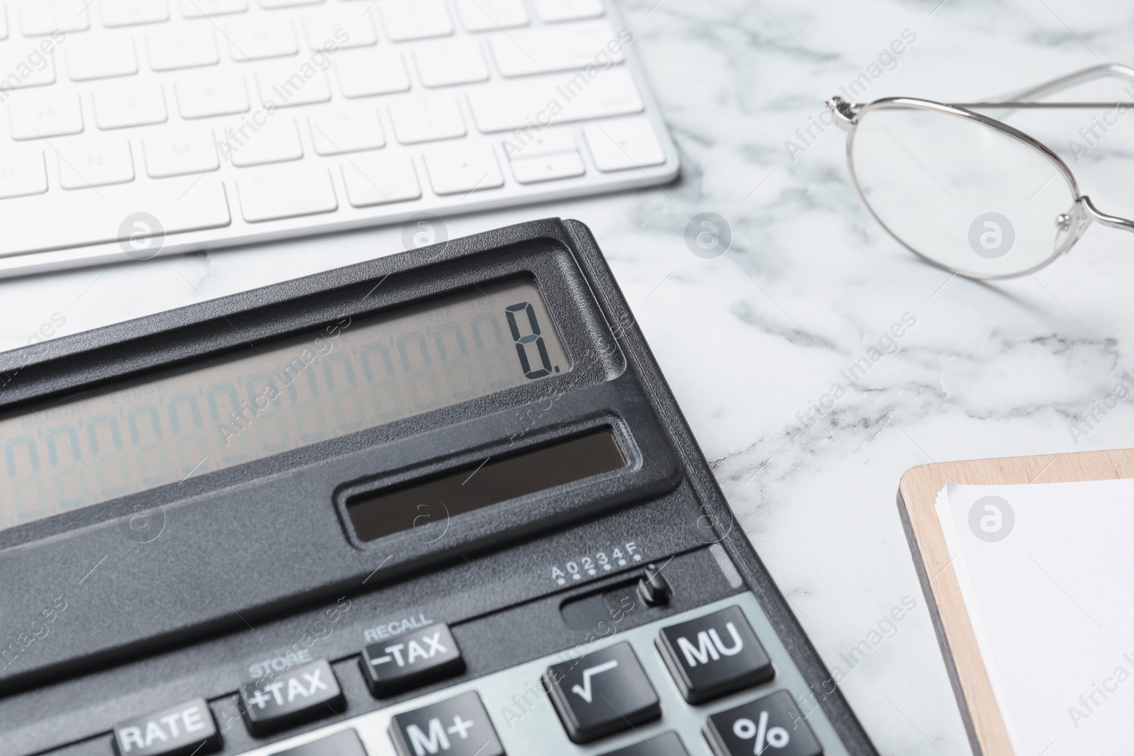 Photo of Calculator, keyboard and glasses on white marble table, closeup. Tax accounting