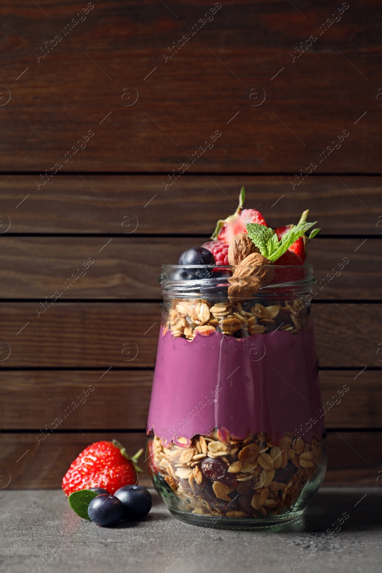 Photo of Delicious acai dessert with granola and berries in glass jar on grey table