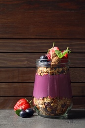 Photo of Delicious acai dessert with granola and berries in glass jar on grey table