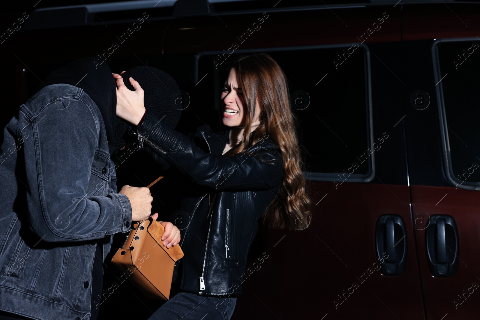 Photo of Woman fighting with thief while he trying to steal her bag near car at night. Self defense concept