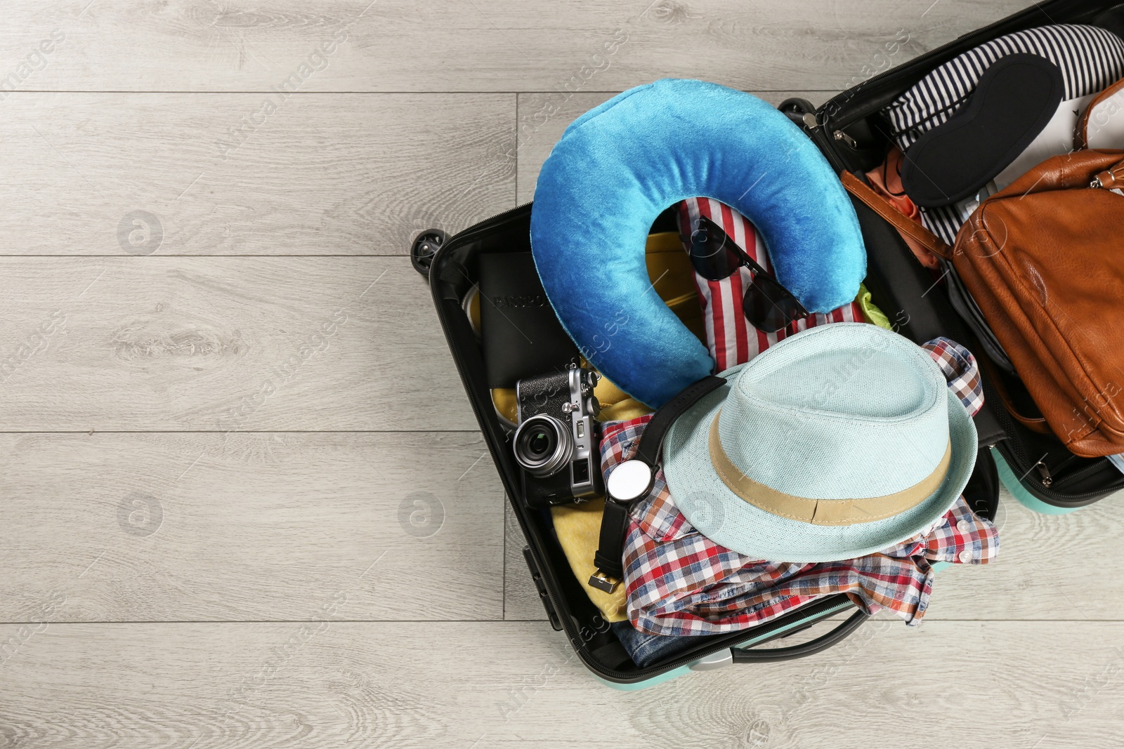 Photo of Opened suitcase with travel pillow and clothes on wooden floor, top view. Space for text