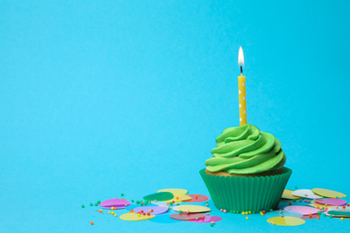 Delicious birthday cupcake with green cream and burning candle on light blue background. Space for text