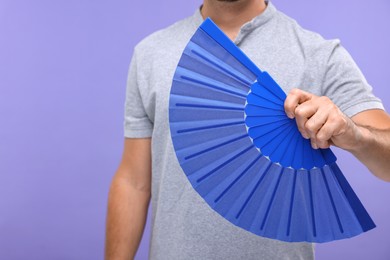 Photo of Man holding hand fan on purple background, closeup. Space for text
