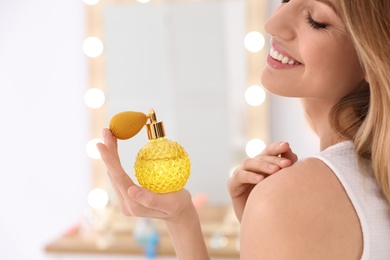 Photo of Young woman with bottle of perfume near mirror indoors