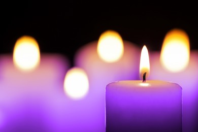 Burning violet candle on black background, closeup. Funeral attributes