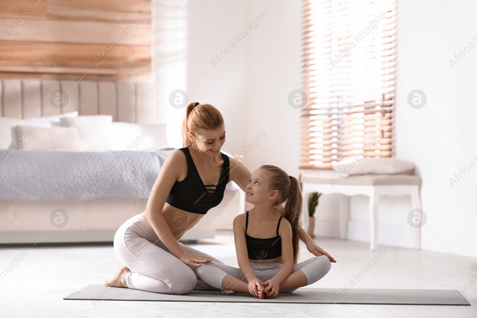 Photo of Mother and daughter in matching sportswear doing yoga together near bed at home