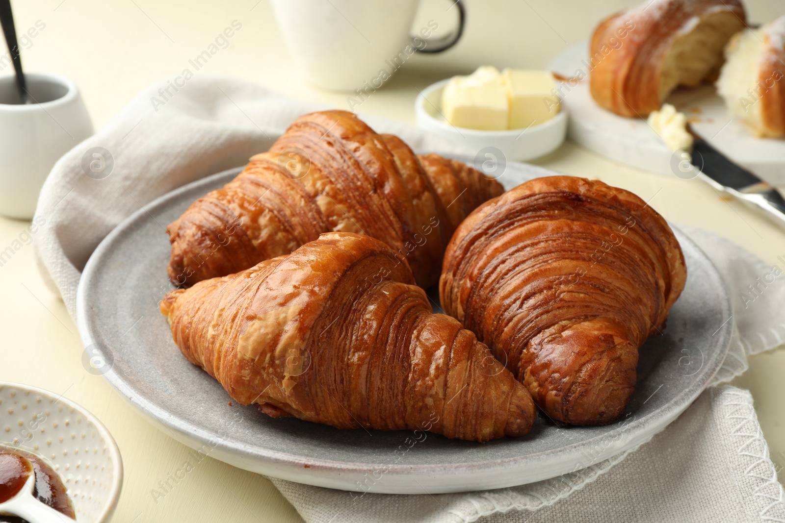 Photo of Plate with tasty croissants on beige table, closeup