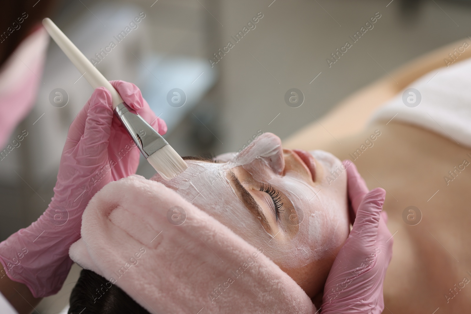 Photo of Cosmetologist applying mask on woman's face in clinic, closeup