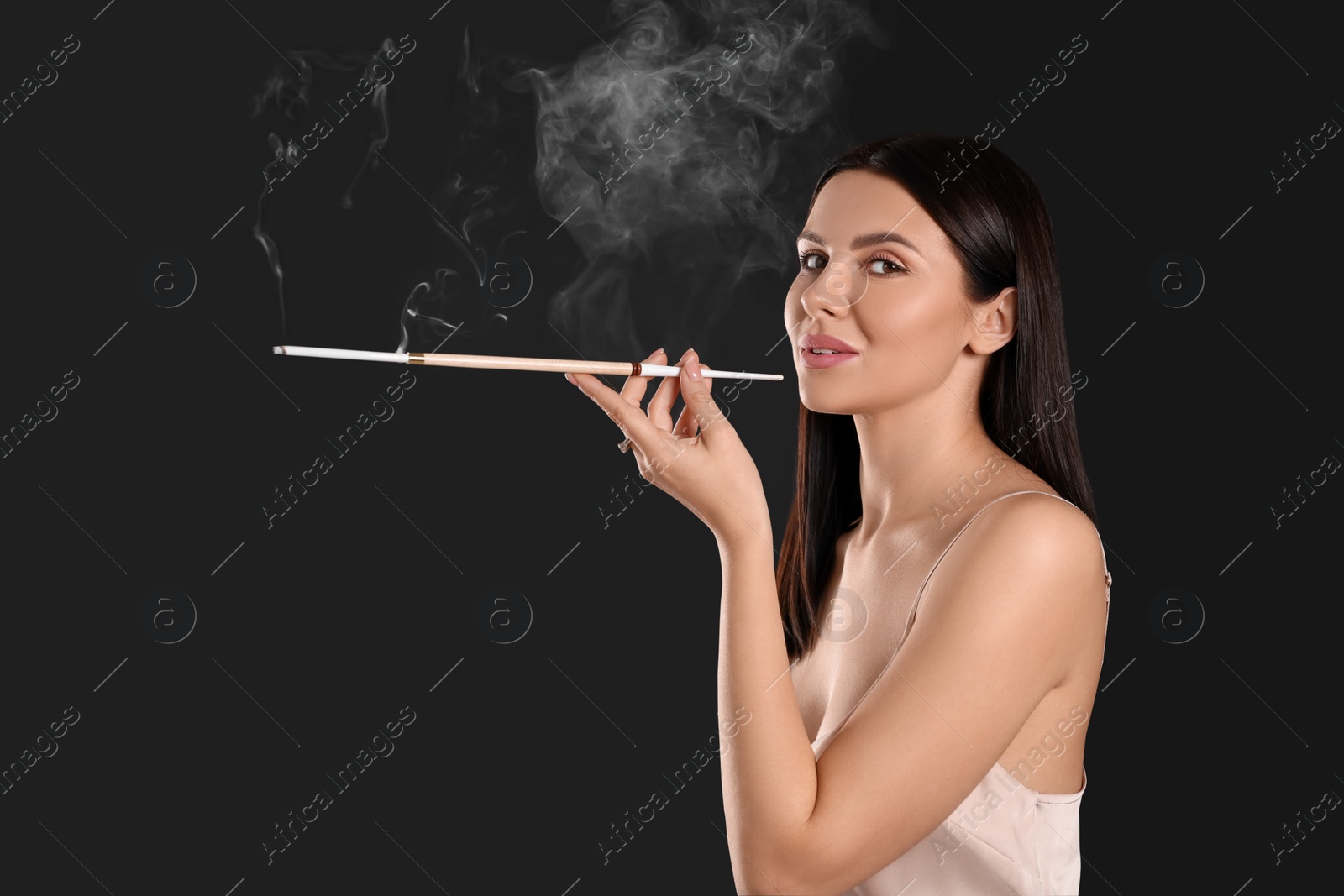 Photo of Woman using long cigarette holder for smoking on black background