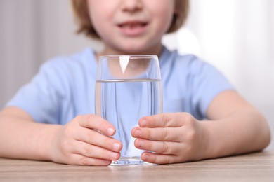 Little boy holding glass of fresh water at wooden table indoors, closeup