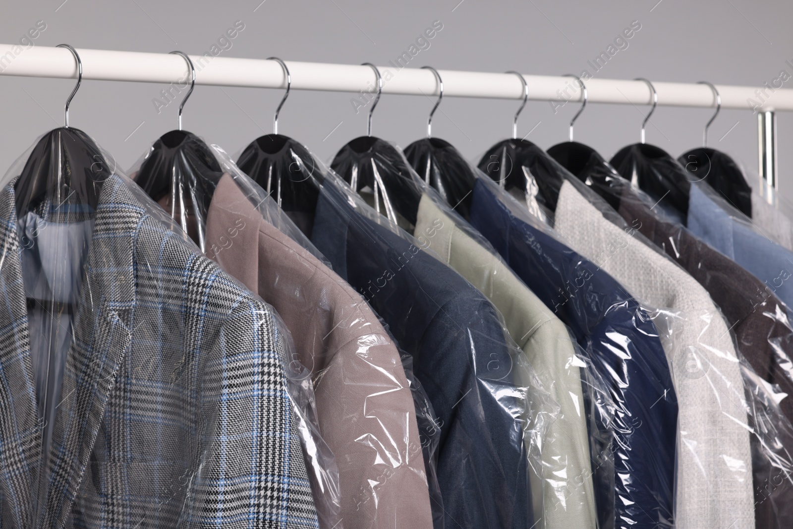 Photo of Dry-cleaning service. Many different clothes in plastic bags hanging on rack against grey background