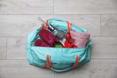 Photo of Sports bag with gym stuff on wooden floor, top view