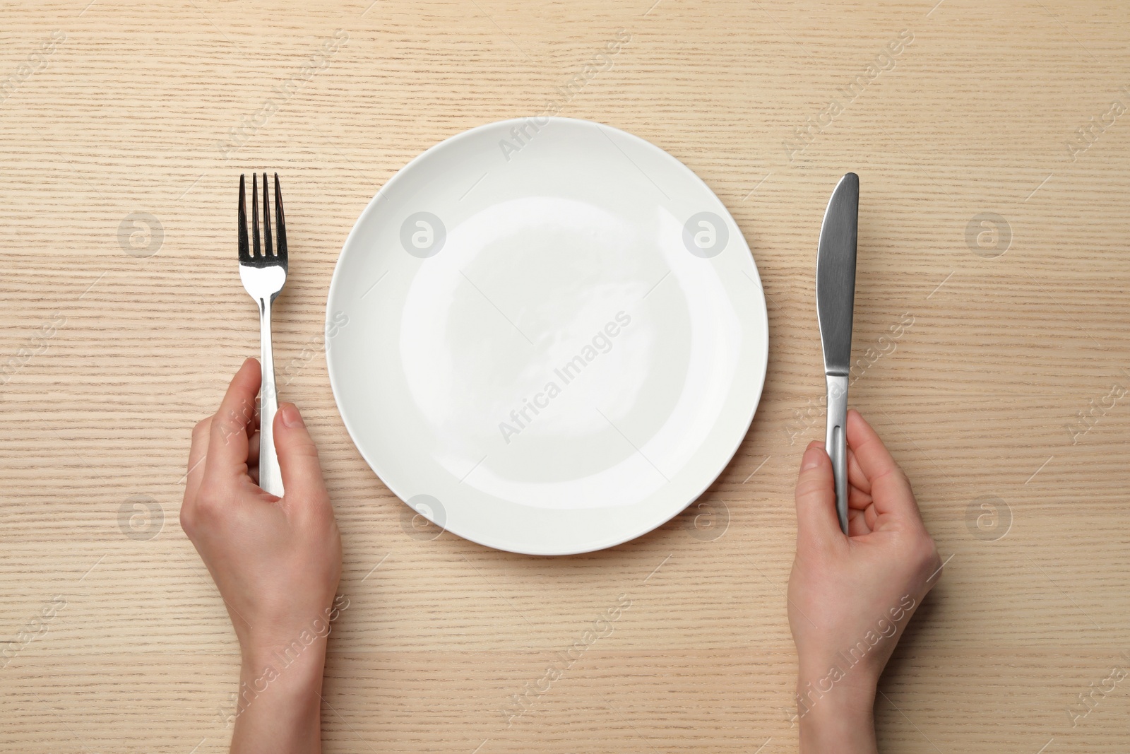 Photo of Woman with empty plate and cutlery at wooden table, top view