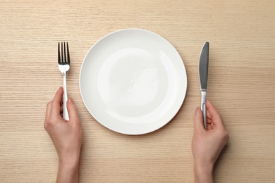 Woman with empty plate and cutlery at wooden table, top view