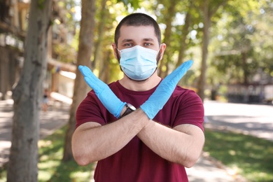 Man in protective face mask showing stop gesture outdoors. Prevent spreading of coronavirus