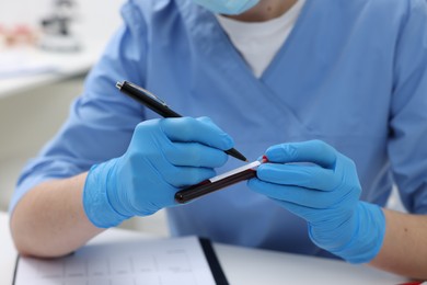 Laboratory testing. Doctor with blood sample in tube at white table indoors, closeup