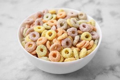 Tasty cereal rings in bowl on white marble table, closeup