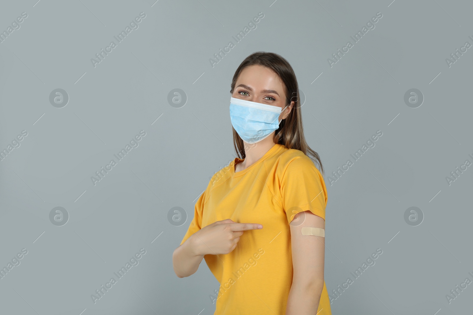 Photo of Vaccinated woman with protective mask showing medical plaster on her arm against grey background