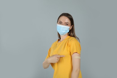 Vaccinated woman with protective mask showing medical plaster on her arm against grey background