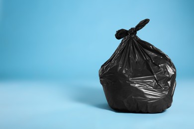 Photo of Black trash bag full of garbage on light blue background, space for text