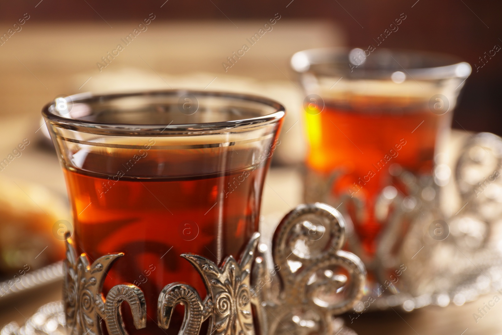 Photo of Glasses of traditional Turkish tea in vintage holders on wooden table, closeup