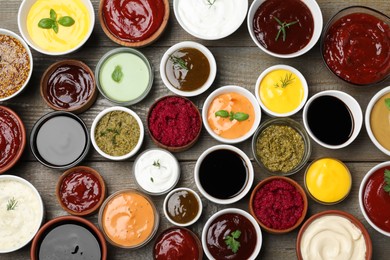 Photo of Many different sauces and herbs on wooden table, flat lay