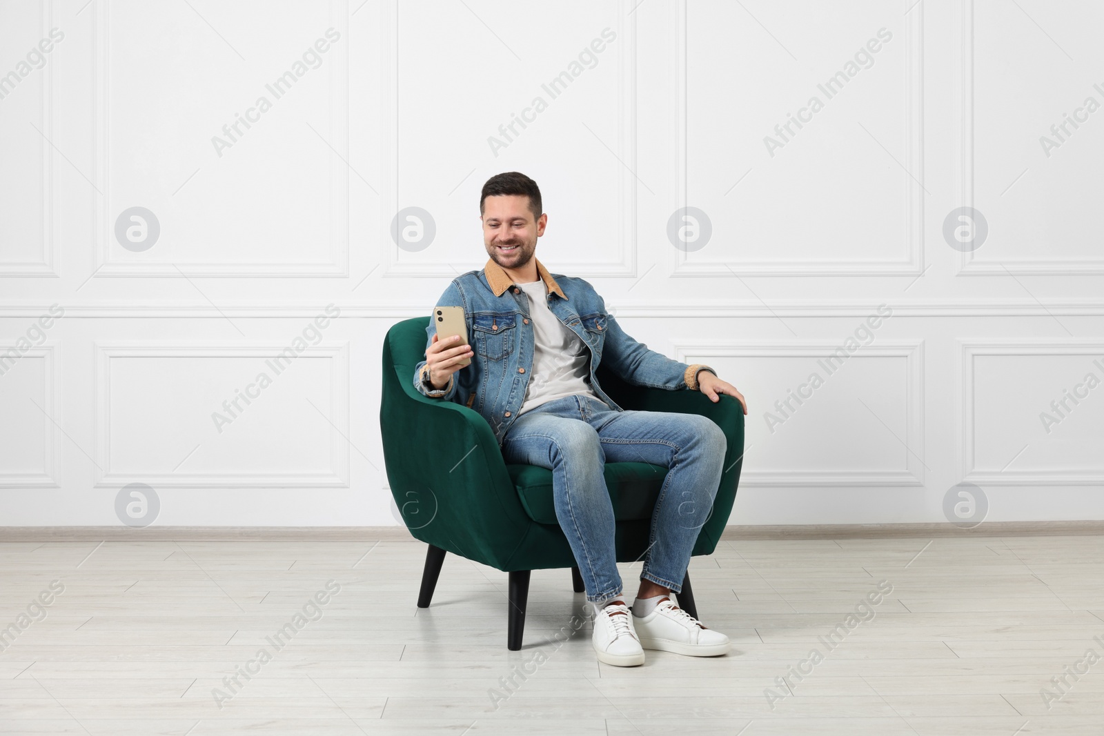 Photo of Happy man sitting in armchair and using smartphone indoors