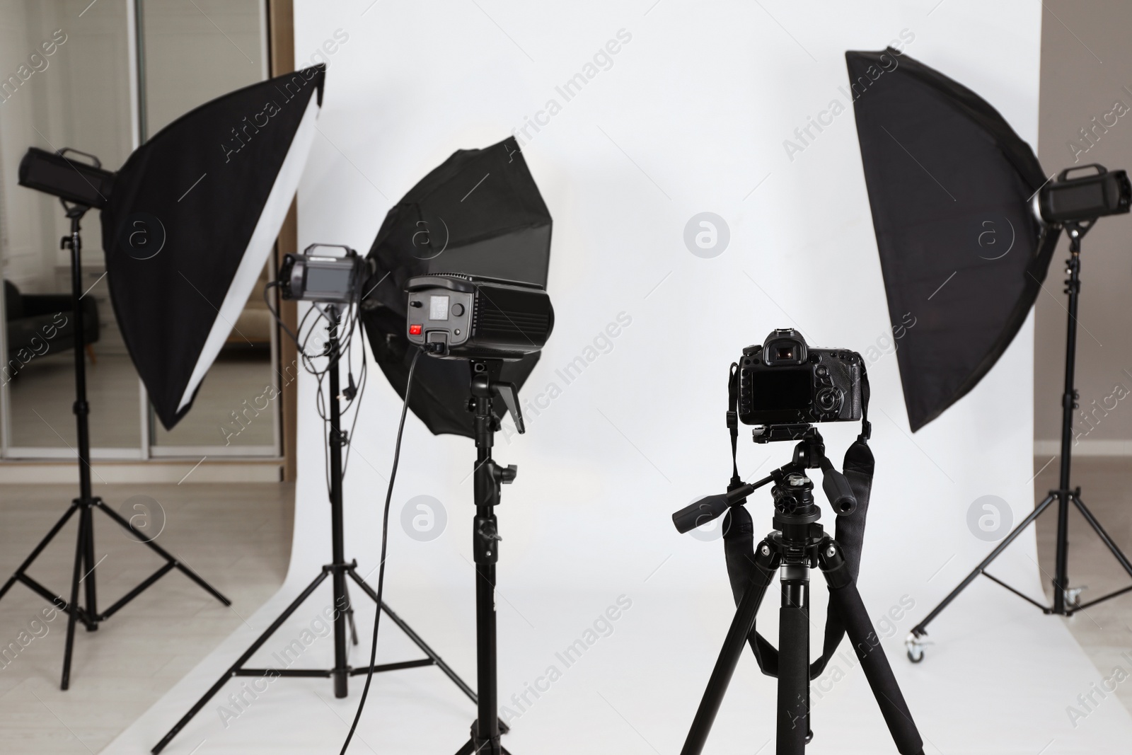 Photo of Tripod with camera and professional lighting equipment in photo studio