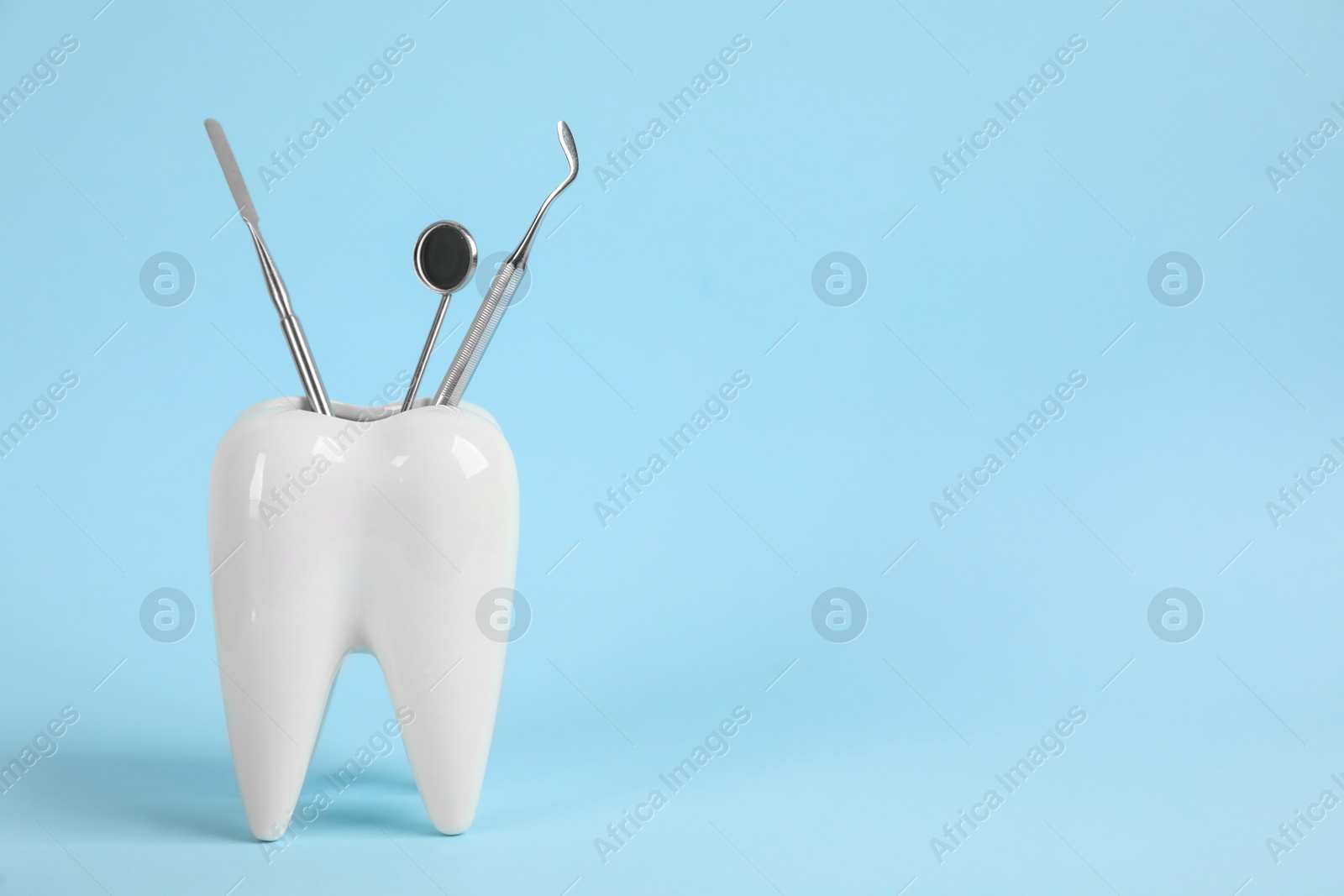 Photo of Tooth shaped holder with set of dentist's tools on light blue background. Space for text