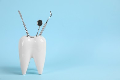 Photo of Tooth shaped holder with set of dentist's tools on light blue background. Space for text