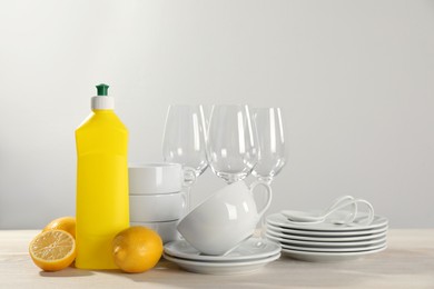 Photo of Set of clean tableware, glasses, dish detergent and lemons on white wooden table against light background