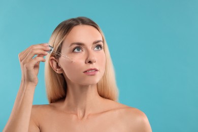 Beautiful woman applying cosmetic serum onto her face on light blue background, space for text