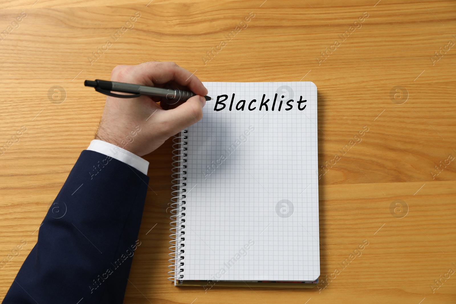 Image of Man writing word Blacklist in notebook at wooden table, top view