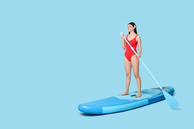 Photo of Happy woman with paddle on SUP board against light blue background, space for text