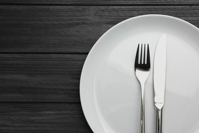 Photo of Clean plate and cutlery on black wooden table, top view