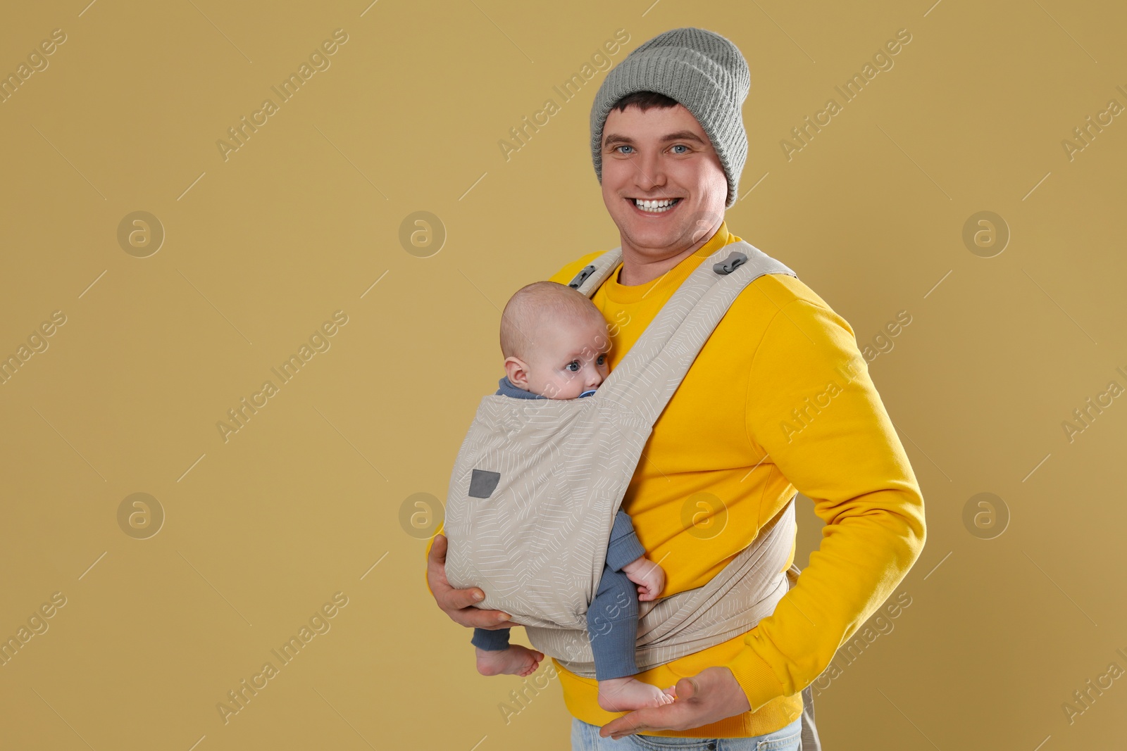 Photo of Father holding his child in sling (baby carrier) on beige background. Space for text