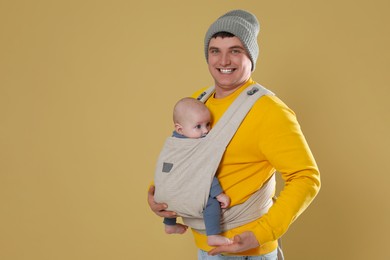 Photo of Father holding his child in sling (baby carrier) on beige background. Space for text