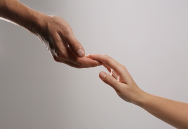 Man reaching for woman's hand on grey background, closeup. Help and support concept