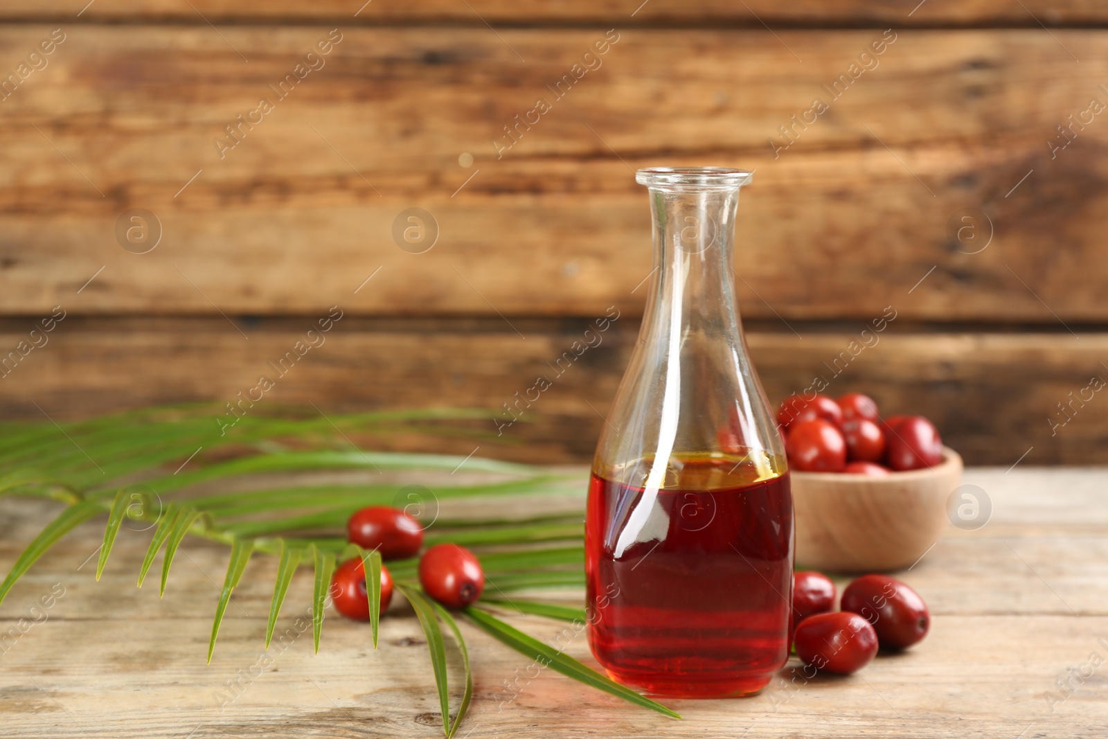 Photo of Palm oil in glass bottle, tropical leaf and fruits on wooden table. Space for text