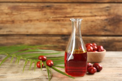 Photo of Palm oil in glass bottle, tropical leaf and fruits on wooden table. Space for text