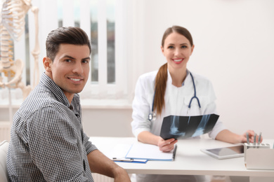 Photo of Orthopedist showing X-ray picture to patient at table in clinic